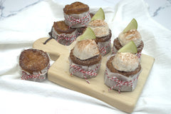 Mini golden apple cakes studded with apple bits, dusted with sugar, alongside muffin pan and baking tools