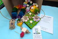 A variety of bird toys spilling out of a cardboard box and onto a blue cloth. Next to it is an itemized receipt and a business card. 