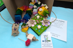 A variety of bird toys spilling out of a cardboard box and onto a blue cloth. Next to it is an itemized receipt and a business card. 