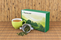 The Tea Smith tea of the month box with a tipped over tea infuser full of tea and a green tea cup full of tea.