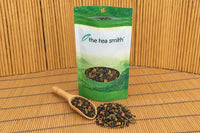 An open Tea Smith club pouch of Applejack Festival, a black and green tea blend with dried apple, with a bamboo scoop of it in front