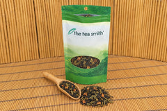 An open Tea Smith club pouch of Applejack Festival, a black and green tea blend with dried apple, with a bamboo scoop of it in front