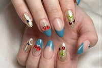 Nude, blue, and gold press-on nails with cherry and rhinestone accents on a hand, combining glossy finishes and detailed nail art for a styl