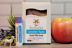 Bar of Lavender Apple goat milk soap sits next to a Lavender Vanilla Lip Butter. A real apple and lavender sprig sit in the background.
