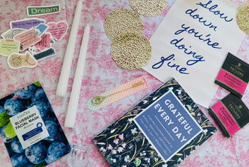 Carefully arranged slow living subscription box contents featured like self-care products, book, cozy home decor, and seasonal accessories