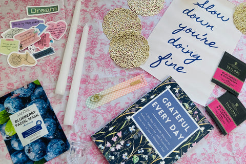 Carefully arranged slow living subscription box contents featured like self-care products, book, cozy home decor, and seasonal accessories