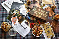 Sample murder mystery box with an assortment of snacks. Showing our branded box, evidence, and clues spread out on table. 