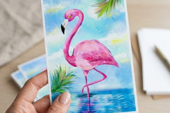 A woman's Hand holding the 4x6 pink flamingo art print with a desk in the background showing scale. 