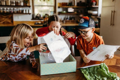 Three happy children excitedly showing off a Wiggle Worms Kit, filled with creative crafting supplies.