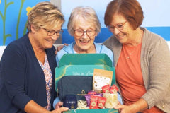 Open Senior Joy Box subscription box featuring snacks, a candle, and socks for aging parents on a cozy table setting