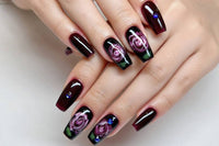 Glossy dark red and black press-on nails with abstract swirl nail art on a hand, featuring long square-shaped tips and a salon-quality high-