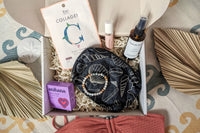 The open Palm People subscription box shows the following products: shower steamer, bracelet, small bag, tanner, perfume, and face mask.