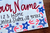 Close-up of a hand-decorated patriotic envelope with red and blue stars, handwritten sample name, address and U.S. mailing details.