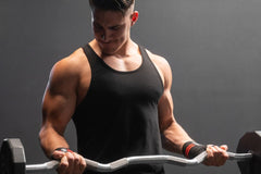 This image shows a fit male model doing bicep curls with a weighted bar while wearing Meat Sportsclub wrist wraps, a Q3 Gainz Box product.