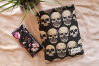 Beige backdrop with a plant, glasses case, and a sewn book cover with multiple skulls around the cover