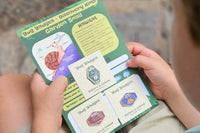 Child holding Bug Badges “Garden Snail” Discovery Hints card with three collectible enamel pins—monthly subscription box for kids