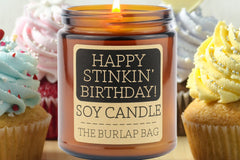 Happy Stinkin' Birthday 9oz soy candle by The Burlap Bag, cupcake scented amber jar in front of frosted birthday cupcakes
