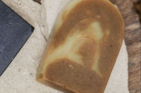 A close up photo of turmeric and lime soap - the color a dark mustard swirled with the lighter lime color on a stone background