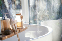 Very luxurious bath with water flowing from the top to down. On the left side are some bath products and a scrub.