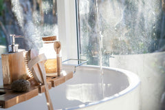 Very luxurious bath with water flowing from the top to down. On the left side are some bath products and a scrub.