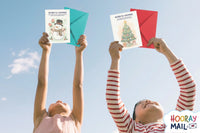 Girl and boy ages 2-5 holding up their monthly Hooray Mail cards from the holiday season with colorful envelopes.