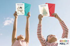 Girl and boy ages 2-5 holding up their monthly Hooray Mail cards from the holiday season with colorful envelopes.