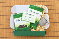 The Tea Smith tea of the month box open with two bags of tea spilling out with information card and tea infuser basket.