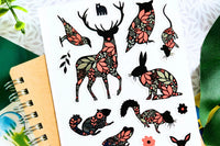 A notebook with a woodland animal sticker sheet.  Animals include a deer, owl, rabbit and more - all decorated with pink and silver foil