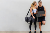 This image shows an attractive female model with a duffel bag standing next to a fit male model holding a closed Gainz Box.