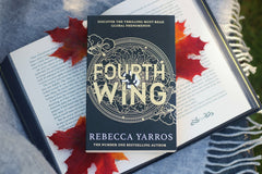 Close up and high quality photo of abook called fourth wing that is a romance book. It is laying on another opened book.