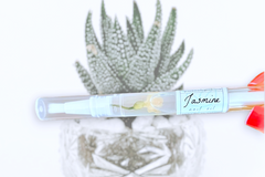 Hand Holding The Jasmine Botanical Nail Pen by Greenmade goods with a Cactus in a White Pot in the Background.