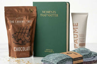 Open Senior Joy Box subscription box featuring snacks, a candle, and socks for aging parents on a cozy table setting