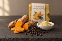 Fresh turmeric root, black peppercorns and a dish of yellow clay in front of the Turmeric & Black Pepper bar in its paper label