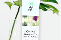 Close up of a Lavender, Jasmine, Rose Cuticle Oil Trio by Greenmade goods against a light background with a plant.