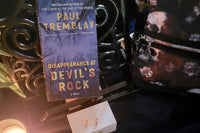 This is a picture of the book titled Disappearance at Devil's Rock with skull earrings on a wooden box, skull purse, and a candle