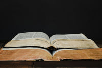 Two very old and used book layered on each other. One of them is white and the other one is yellow. Background is pitch black.
