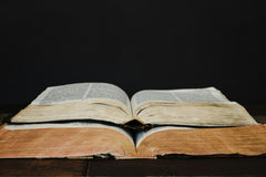 Two very old and used book layered on each other. One of them is white and the other one is yellow. Background is pitch black.