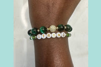 Handmade encouragement bracelet with rich green stone beads, clear and green faux crystal accents, and white letter beads spelling “STRONG” 