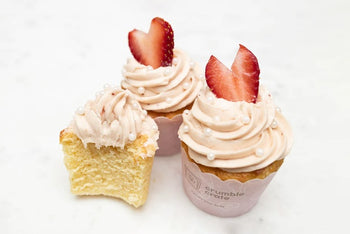 Bright lemon cupcakes topped with pink strawberry buttercream swirls and white sugar pearls in a baking kit setup
