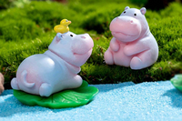 This is a photograph of a tiny miniature hippo laying on a green lily pad.  There is a yellow rubber ducky on the hippos head.   