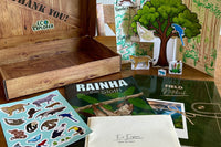 The Eco Explorer field notebook, comic book, sticker sheet, box, envelopes, and paper rainforest diorama spread out on a wooden table.