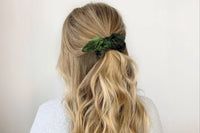a green velvet bow scrunchie used in a loose casual half up style on blonde hair as an example of our scrunchies