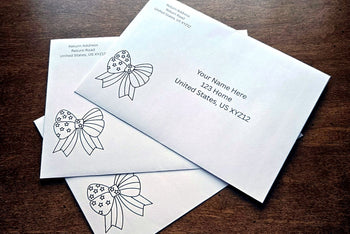 Three white envelopes with printed sample U.S. mailing addresses and black outline patriotic bow designs arranged on a wooden table.