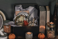 open black box next to books and candles containing a book, jar, feathers, candles and other witchy items