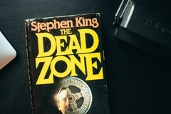 Close up photo of a book called the dead zone from stephen king and a black object in top right corner