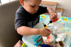 Child engaged in hands-on sensory bin play with laminated learning materials. Child engaged in pretend snow cone play.