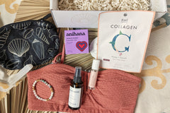 These Palm People box products are displayed on a beach towel: shower steamer, bracelet, small bag, tanner, perfume, and face mask.