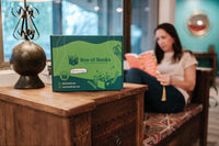 A woman reading a book in a cozy nook with a Box of Books subscription box nearby