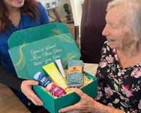 Elderly woman smiling while opening a thoughtful gift box filled with meaningful items
Senior enjoying curated comfort products