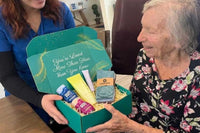 Elderly woman smiling while opening a thoughtful gift box filled with meaningful items
Senior enjoying curated comfort products